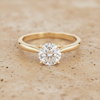 Ultra high-resolution product photo of a gold ring with a diamond on.  
Minimal, premium style on a warm stone background.  
Clean studio lighting with gentle highlights.  
Square format (1:1).  
Ring centred, filling about 65% of the frame.  
Looks professionally restored and like new.  
No text, no logos, no people.